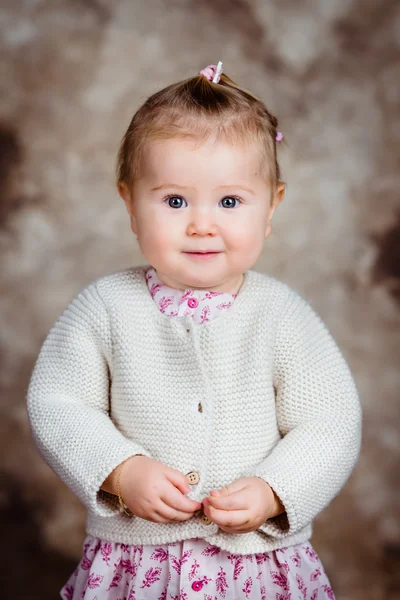 Portrait of beautiful blond little girl with big grey eyes and plump cheeks looking at camera. Studio portrait on brown grunge background — Stock Photo, Image