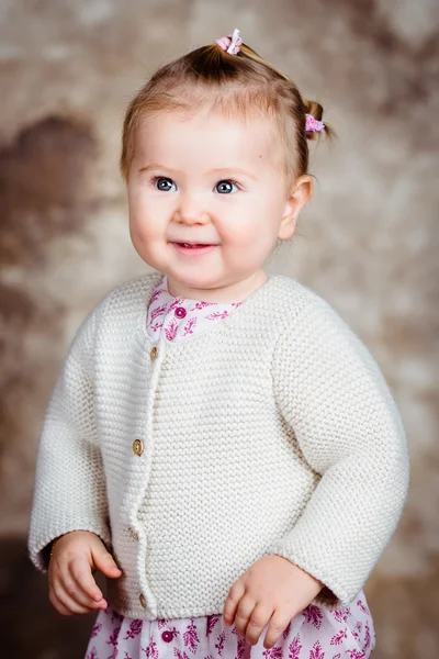 Portrait of beautiful smiling blond little girl with big grey eyes and plump cheeks. Studio portrait on brown grunge background — Stock Photo, Image