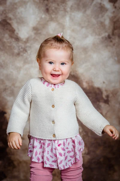 Cute little girl with blond hair and grey eyes laughs and dances. Children's fashion. Studio portrait on brown grunge background — Stock Photo, Image