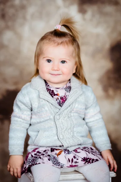 Adorable niña con el pelo rubio sentado en la silla blanca y sonriendo —  Fotos de Stock