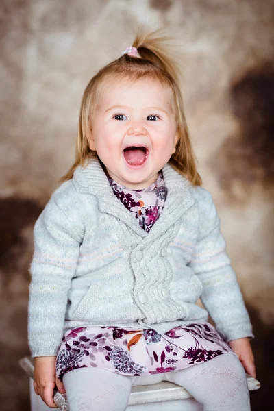 Sevimli küçük kız sarışın saçlı beyaz sandalyede oturan ve gülüyor — Stok fotoğraf