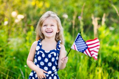 Uzun kıvırcık sarı saçlı bir Amerikan bayrağı tutarak, sallayarak ve güneşli günde yaz parkta gülüyor sevimli küçük kız. Bağımsızlık günü, bayrak günü kavramı