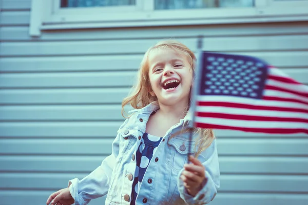 Söt liten flicka med långt lockigt blont hår skrattar och vinkar amerikanska flaggan. Självständighetsdagen, flagga dag koncept. Vintage och retro färger. Instagram filter — Stockfoto