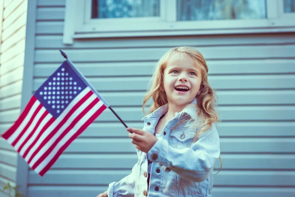 Niña bonita con el pelo largo rubio rizado sonriendo y ondeando bandera americana. Día de la Independencia, concepto del Día de la Bandera. Colores vintage y retro. Filtros Instagram Imagen de archivo