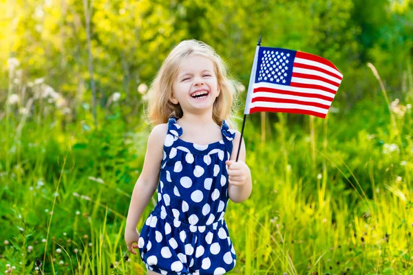 Schattig lachen meisje met lang krullend blond haar bedrijf Amerikaanse vlag en zwaaien het op zonnige dag in zomer park. Independence Day, dag van de vlag concept — Stockfoto