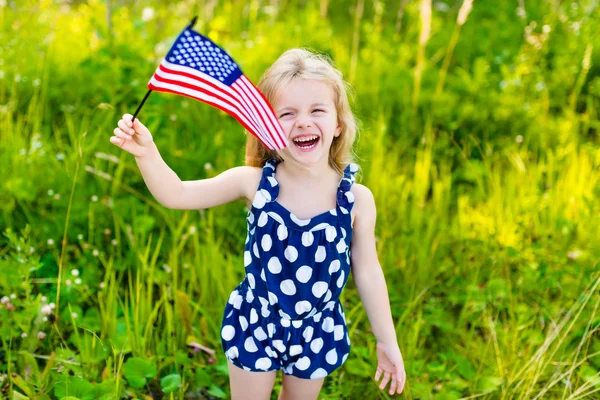 Lachen meisje met lang krullend blond haar bedrijf Amerikaanse vlag en zwaaien het, buiten portret op zonnige dag in zomer park. Independence Day, dag van de vlag concept Stockfoto