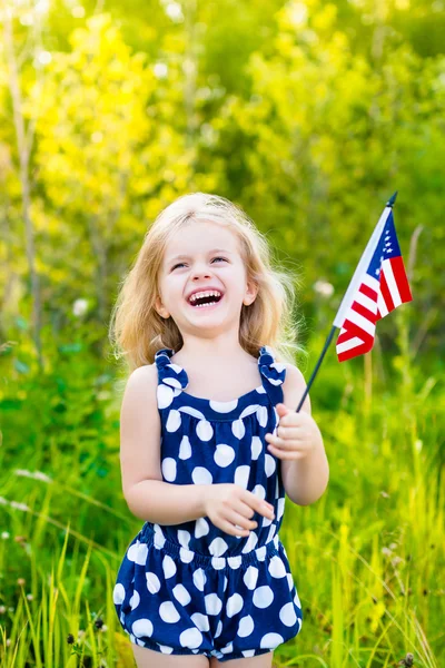 Riéndose niña rubia con el pelo rizado largo sosteniendo bandera americana, retrato al aire libre en el día soleado en el parque de verano. Día de la Independencia, concepto del Día de la Bandera Fotos de stock libres de derechos