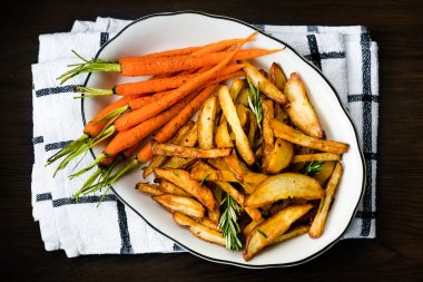 Kavrulmuş sebze biberiye ve karabiber ile terbiyeli. Fırında bebek havuç ve patates karanlık masada beyaz kase. Sağlıklı vejetaryen yemek, lezzetli vegan gıda