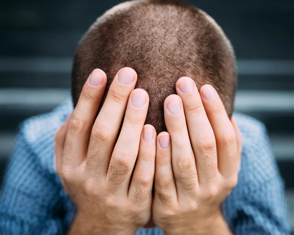 Closeup portrait of despaired young man covering his face with hands. Selective focus on hands. Sadness, despair, tragedy concept — Stock Photo, Image