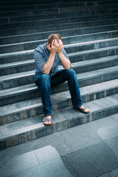 Retrato ao ar livre do jovem desesperado cobrindo seu rosto com as mãos sentadas nas escadas. Sentimentos de tristeza, desespero e tragédia — Fotografia de Stock