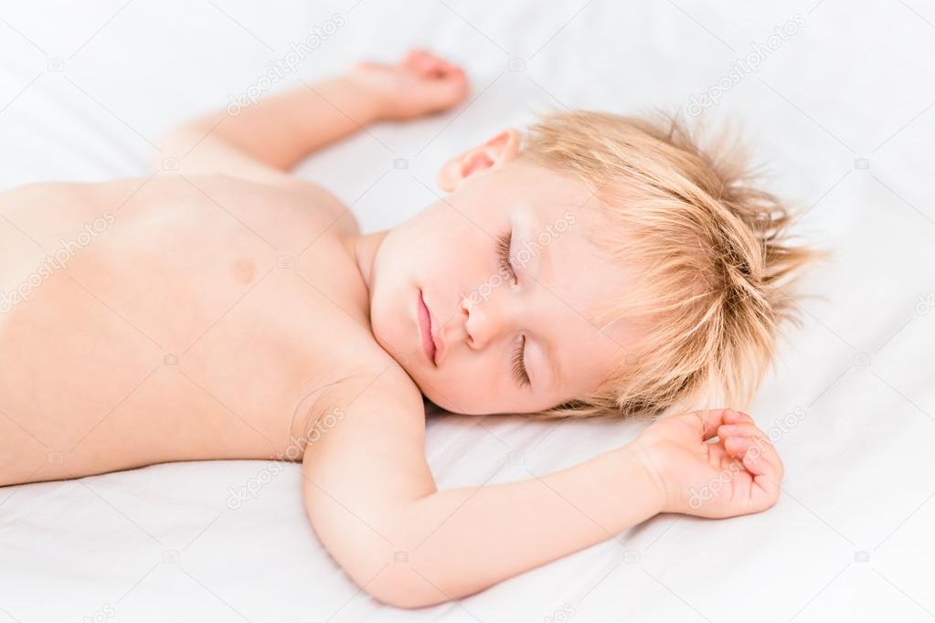 Close-up portrait of little boy with blond hair sleeping on white bad. Carefree childhood concept
