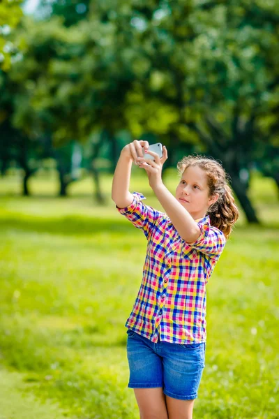 Mooie tienermeisje nemen foto met smartphone in zonnige dag in zomer park. Tiener meisje dat neemt selfie met smartphone Rechtenvrije Stockafbeeldingen