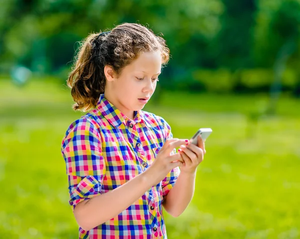 Adolescente sorprendida en ropa casual con teléfono inteligente en la mano, mirando a la pantalla, leyendo un mensaje, usando Facebook, mensajes de texto y chat Fotos de stock libres de derechos