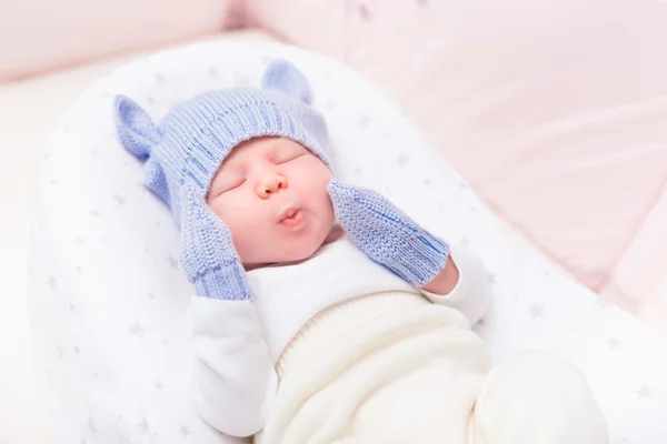 Cute little baby wearing knitted blue hat with ears and mittens lying in beautiful cradle with closed eyes and making funny face. Security and childcare concept — Stock Photo, Image