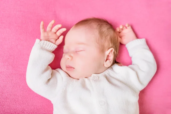 2 week old baby with closed eyes wearing knitted white clothes lying on pink plaid. Sweet little baby sleeping on pink sofa. Security and childcare concept. Selective focus on eye — Stok fotoğraf