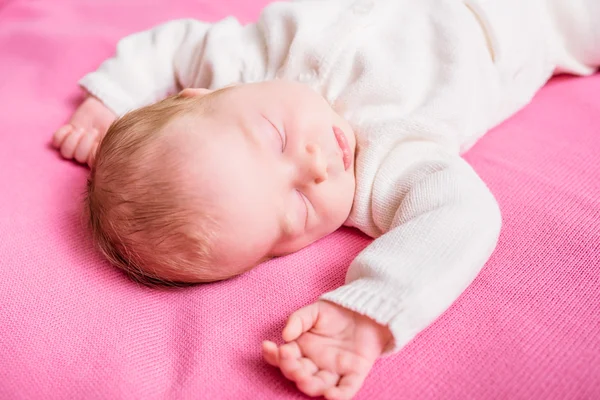 Sweet little baby with closed eyes wearing knitted white clothes lying on pink plaid. 2 week old baby sleeping on pink sofa. Security and childcare concept — Stock Photo, Image