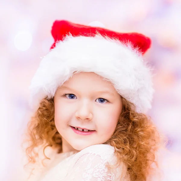 Retrato de cerca de una hermosa niña pelirroja con el pelo rizado largo usando el sombrero de Navidad de Papá Noel. Concepto de celebración de Navidad y Año Nuevo — Foto de Stock