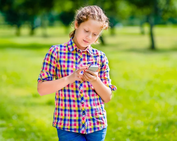 Bella adolescente sorridente in abiti casual con smartphone in mano, guardando lo schermo, leggendo un messaggio, utilizzando Facebook, sms e chat — Foto Stock