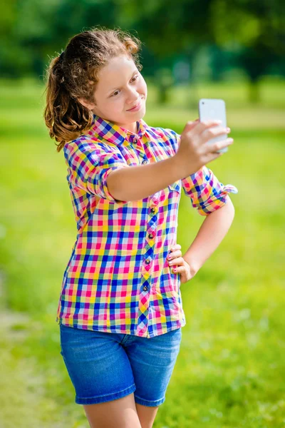 Lovely smiling girl posing and taking selfie with smartphone in sunny day in summer park. Teenage girl taking picture with smartphone — Stock Photo, Image