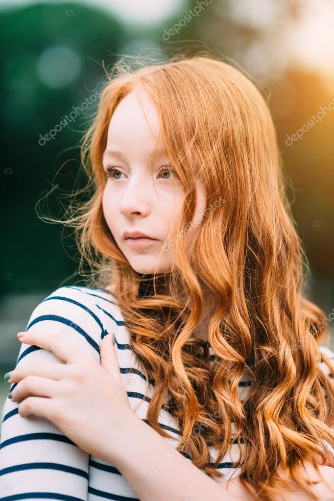 A beautiful teenage girl with long curly ginger hair and green eyes hugging herself in summer park. Outdoor of attractive red-haired young in evening at sunset Stock Photo ©aquamila