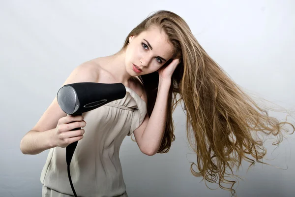 A menina brinca com o secador de cabelo com o cabelo Fotografias De Stock Royalty-Free