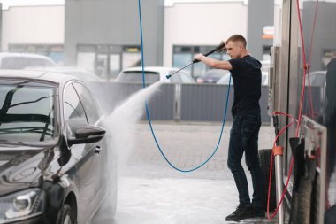 Araba yıkama. Yüksek basınçlı su kullanarak arabayı temizlemek. Adam dışarıda arabasını yıkıyor.