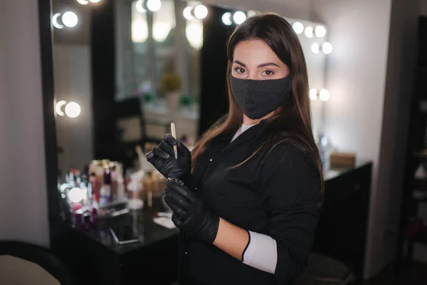 Портрет профессиональной женщины-мастера бровей в черном халате с черными перчатками и черной защитной маской используют кисть и хну для бровей — стоковое фото