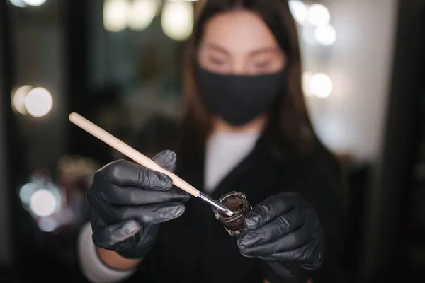 Close-up of brow master hands in black gloves using brush and henna for eyebrows