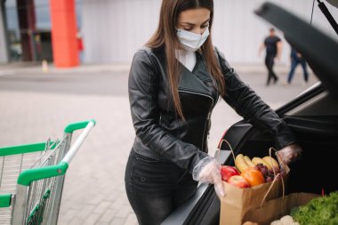Çekici genç bir kadının market alışverişini tramvaydan araba kamyonuna taşıması. Enfeksiyonu önlemek için sosyal güvenlik mesafesi, yüz maskesi, tek kullanımlık eldivenler. Yiyecek.