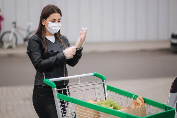 Μια νεαρή ελκυστική γυναίκα να πηγαίνει ψώνια από ένα σούπερ μάρκετ από το τρόλεϊ στο φορτηγό. Κοινωνική αποστασιοποίηση για προστασία, μάσκα προσώπου, γάντια μιας χρήσης για την πρόληψη μόλυνσης. Αγορές τροφίμων κατά — Φωτογραφία Αρχείου