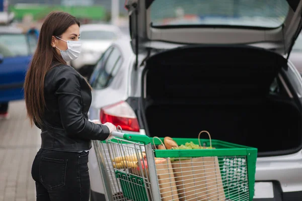 Молодая привлекательная женщина берет продукты из супермаркета от тележки до грузовика. Социальное дистанцирование для защиты, маска для лица, одноразовые перчатки для предотвращения инфекции. Продовольствие во время — стоковое фото