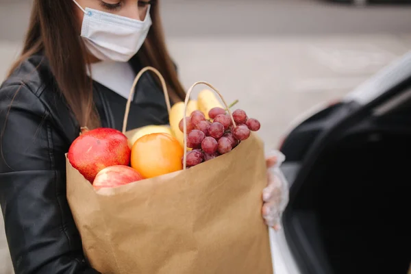 Κοντινό πλάνο του παντοπωλείου στις γυναίκες χέρι από το φορτηγό αυτοκίνητο. Γυναίκα με προστατευτική μάσκα και γάντια μιας χρήσης. Φρέσκα φρούτα σε οικολογικό πακέτο. Ψώνια τροφίμων κατά τη διάρκεια της καραντίνας Coronavirus Covid-19 — Φωτογραφία Αρχείου