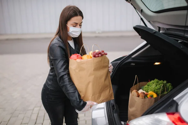 Παντοπωλεία στα θηλυκά χέρι από το φορτηγό αυτοκίνητο. Γυναίκα με προστατευτική μάσκα και γάντια μιας χρήσης. Φρέσκα φρούτα σε οικολογικό πακέτο. Ψώνια τροφίμων κατά τη διάρκεια της καραντίνας Coronavirus Covid-19 — Φωτογραφία Αρχείου