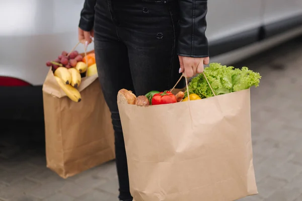 在一个生态工艺包装超市里的食品杂货检疫期间运送食品.纸袋里塞满了新鲜食物.女人在车边拿着两个包裹.四.后续行动 — 图库照片