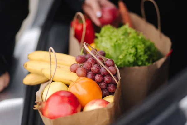 Крупный план продуктов в эко-упаковке в багажнике автомобиля. Руки женщины упаковки овощей и фруктов после доставки в супермаркет — стоковое фото