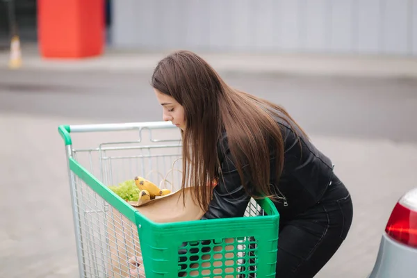 一个过程，年轻迷人的女人把食品从超市从推车到汽车卡车。检疫期间的食品采购。笑得开心的女人 — 图库照片
