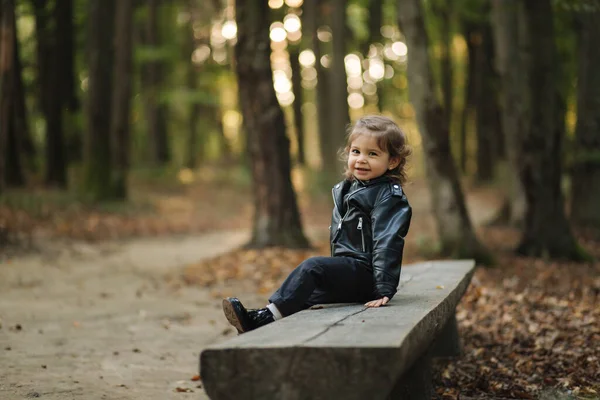Linda niña sentada en el banco en el bosque. Niño feliz caminando al aire libre — Foto de Stock