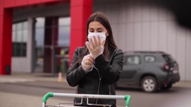 Seorang wanita muda yang menarik mengambil bahan makanan dari supermarket dari troli ke truk mobil. Jarak sosial untuk perlindungan, masker wajah, sarung tangan sekali pakai untuk mencegah infeksi. Belanja makanan selama — Stok Video