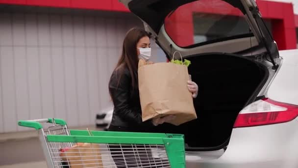 Um processo de jovem mulher atraente levando mantimentos de um supermercado do carrinho para caminhão de carro. Distanciamento social para proteção, máscara facial, luvas descartáveis para prevenir a infecção. Alimentos — Vídeo de Stock