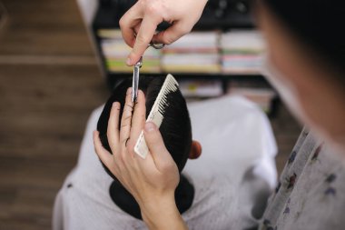 Berber dükkanında saçını makas kesen bir adam. Berber makas kullanır ve koronavirüs salgını sırasında maske takar. Profesyonel berber evde çalışıyor. Covid-19 karantina