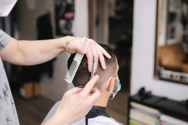 Al hombre le cortaron el pelo con tijera en la peluquería. Peluquero usar tijera y usar máscara durante la pandemia de coronavirus. Trabajo de peluquero profesional en casa. Cuarentena de Covid-19 — Foto de Stock