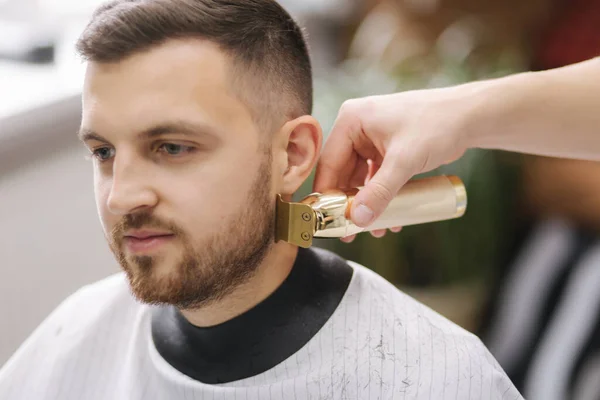 Professionele kapper maakt gebruik van een tondeuse voor fringing baard voor een knappe man in kapperszaak — Stockfoto