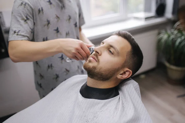 Peluquería profesional utiliza un cortador de pelo para flecos cabello para un hombre portador guapo. Peluquería — Foto de Stock