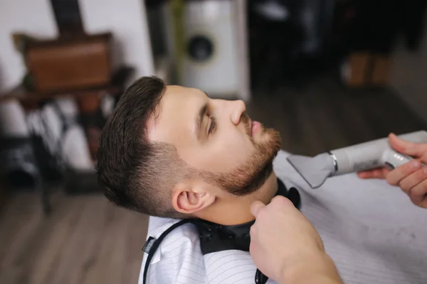 Cabeleireiro profissional usa um cortador de cabelo para franzir o cabelo para um homem de barba bonito. Barbearia — Fotografia de Stock