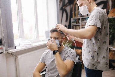 Berber dükkanında saçını makas kesen bir adam. Berber makas kullanır ve koronavirüs salgını sırasında maske takar. Profesyonel berber evde çalışıyor. Covid-19 karantina