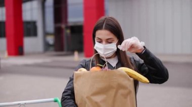 Kamyonetin yanında kadın kıyafetleri var. Koruyucu maskeli ve tek kullanımlık eldivenli kadın. Eko paket 'de taze meyve. Coronavirus Covid-19 karantinası sırasında yiyecek alışverişi. Kadın elmayı hisset