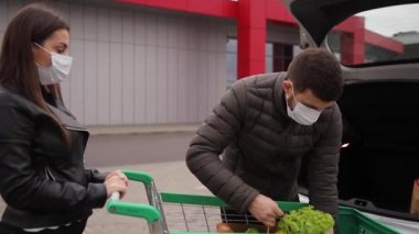 Karantina sırasında marketten ya da süpermarketten yiyecek aldıktan sonra koruyucu maskeli koca ve karısı. Yan görüş. Coronavirus Covid-19 karantinası sırasında yiyecek alışverişi