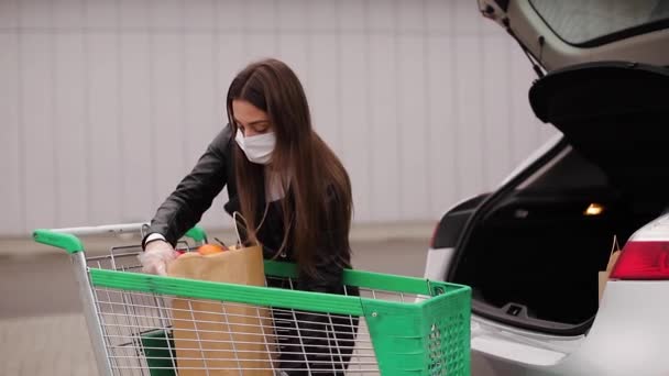 Um processo de jovem mulher atraente levando mantimentos de um supermercado do carrinho para caminhão de carro. Distanciamento social para proteção, máscara facial, luvas descartáveis para prevenir a infecção. Alimentos — Vídeo de Stock