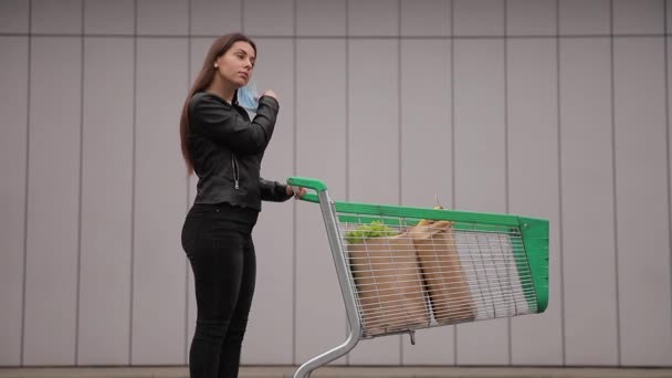 若い魅力的な女性がスーパーマーケットから車へのトロリーフードで歩く — ストック動画