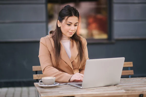 Jovem mulher de negócios sentada no terraço por café com laptop. Mulher a beber café e a trabalhar ao ar livre. uso feminino telefone e notebook — Fotografia de Stock